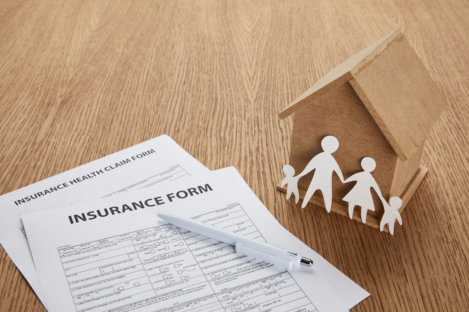 close-up view of insurance form, insurance health claim form, pen, small house and paper cut family